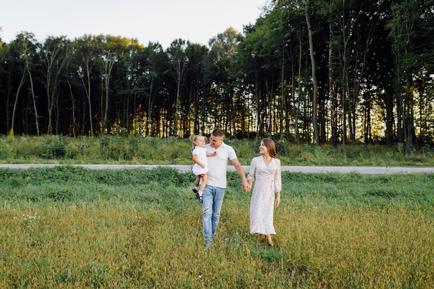 Familia feliz en un parque en verano otoño. Madre, padre y bebé juegan en la naturaleza bajo los rayos del sol