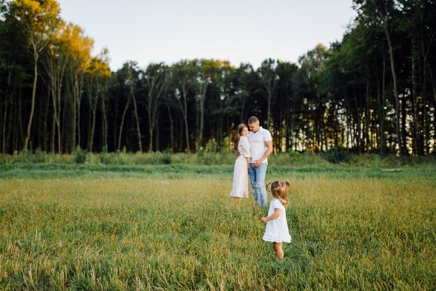 Familia feliz en un parque en verano otoño. Madre, padre y bebé juegan en la naturaleza bajo los rayos del sol