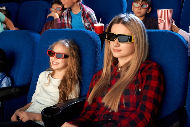 Familia feliz pasar tiempo juntos en el cine. Madre joven atractiva y pequeña hija riendo con anteojos 3d mientras ve la película