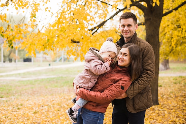 Familia feliz de pie y sonriendo en el jardín de otoño