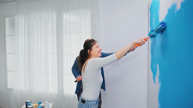 Familia feliz pintando la pared del apartamento con pintura azul con un cepillo de rodillo. Decoración y renovación del hogar en acogedor piso, reparación y renovación.