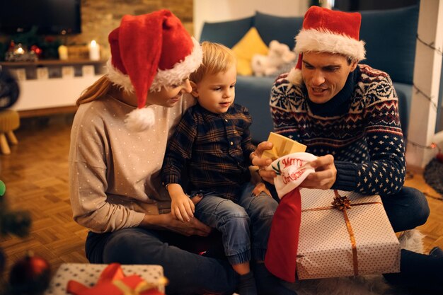 Familia feliz poniendo un regalo en el calcetín de Navidad por la noche en casa