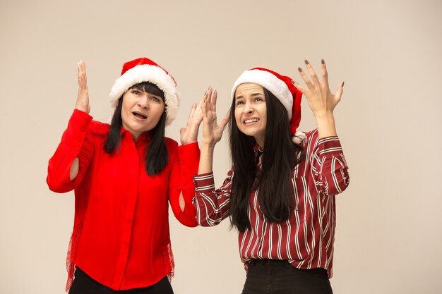 Familia feliz en la presentación del suéter de la Navidad. Disfrutando de abrazos de amor, gente de vacaciones. Mamá y hija sobre un fondo gris en el estudio