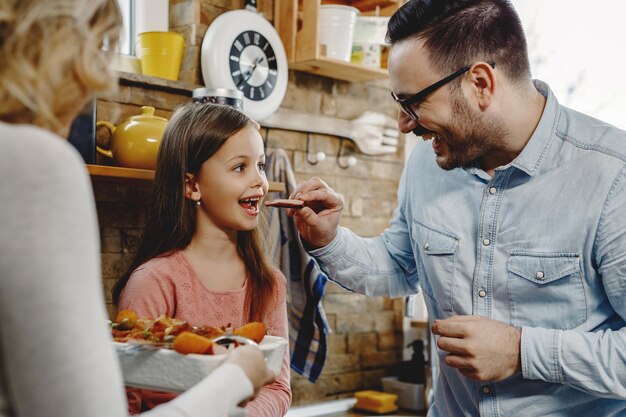 Familia feliz probando comida en la cocina El padre está alimentando a la niña