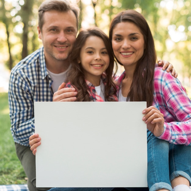 Foto gratuita familia feliz que lleva a cabo el cartel blanco en blanco en parque