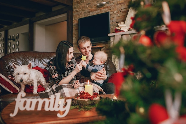 Familia feliz sentada en el sofá con un árbol de navidad desenfocado delante y la palabra 