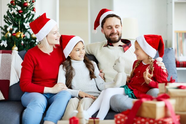 Familia feliz sentado en el sofá y desenvolver regalos de Navidad