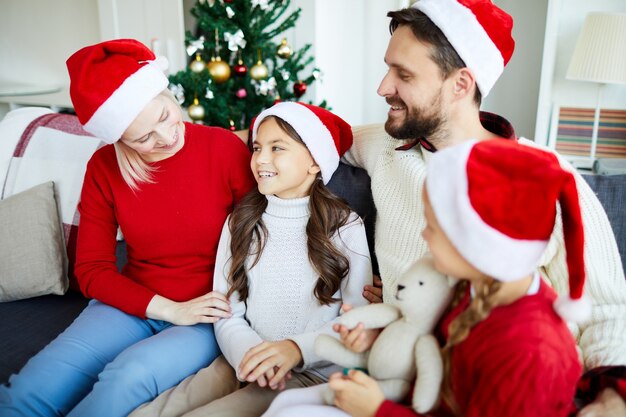 Familia feliz sentado en el sofá y desenvolver regalos de Navidad