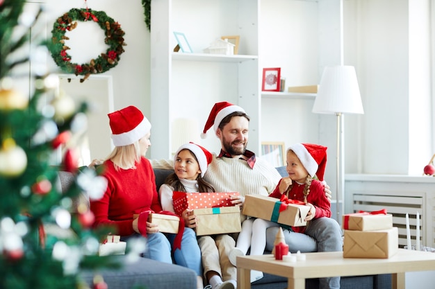 Familia feliz sentado en el sofá y desenvolver regalos de Navidad