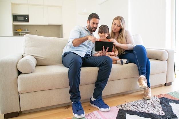 Foto gratuita familia feliz sentado en el sofá, usando la aplicación en línea en la tableta, mirando la pantalla, viendo películas juntos.