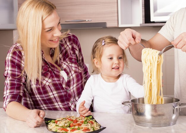 Familia feliz y su pequeña hija preparando espaguetis caseros en la encimera de la cocina