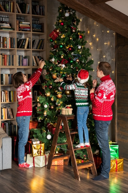 Familia feliz de tiro completo decorando el árbol