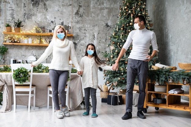 Foto gratuita una familia feliz usa máscaras médicas debido al coronavirus covid-19 cerca del árbol de navidad. vacaciones de navidad.