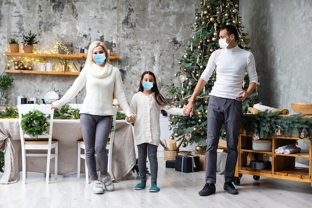 Una familia feliz usa máscaras médicas debido al coronavirus COVID-19 cerca del árbol de Navidad. vacaciones de navidad.