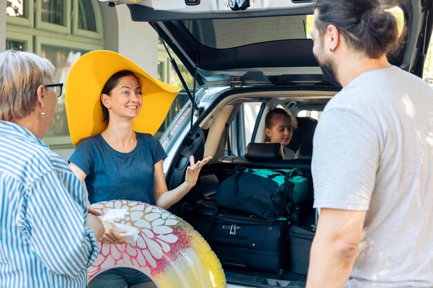 Familia feliz viajando de vacaciones junto al mar, saliendo con maleta y equipaje en el maletero del auto. Niña, padres y abuelos que van al destino marítimo con automóvil, para viajar de vacaciones.