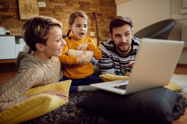 Familia feliz viendo una película en la computadora portátil mientras come palomitas de maíz en casa