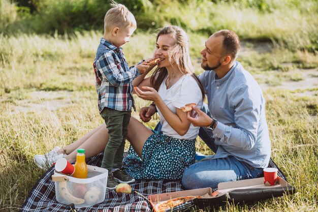 Familia haciendo un picnic y comiendo pizza en el parque