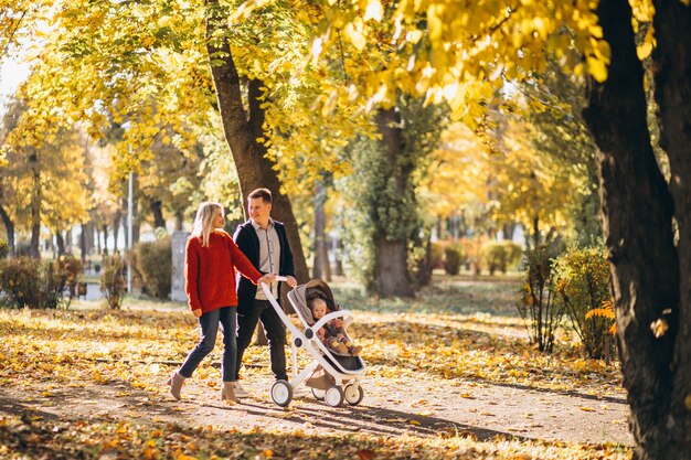 Familia con hija en un cochecito caminando por un parque de otoño