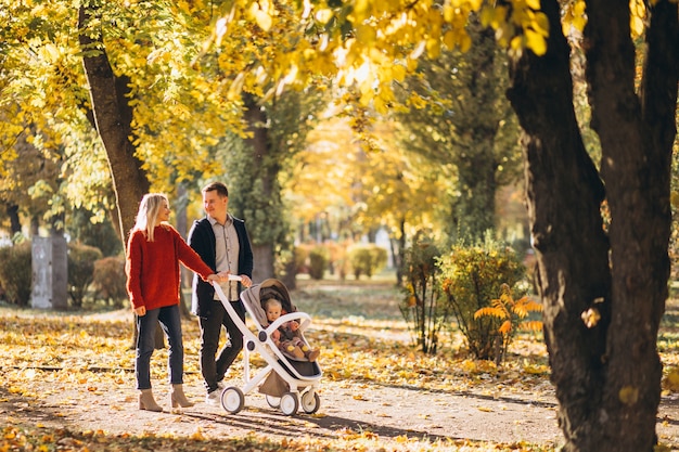 Familia con hija en un cochecito caminando por un parque de otoño