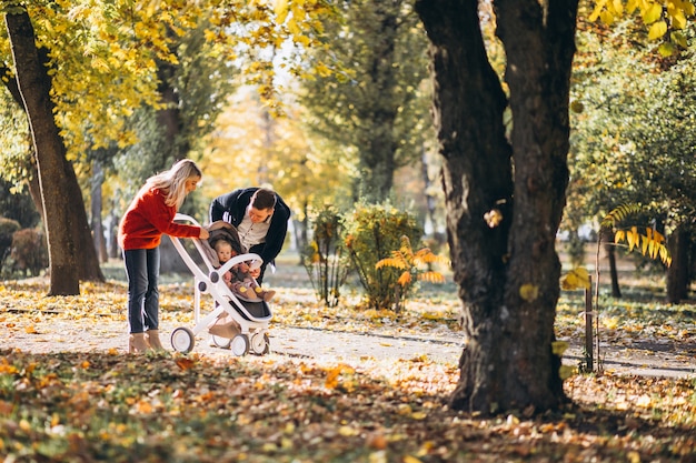 Familia con hija en un cochecito caminando por un parque de otoño