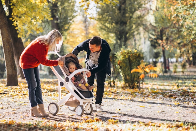 Familia con hija en un cochecito caminando por un parque de otoño