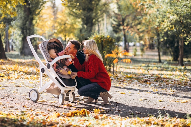 Familia con hija en un cochecito caminando por un parque de otoño