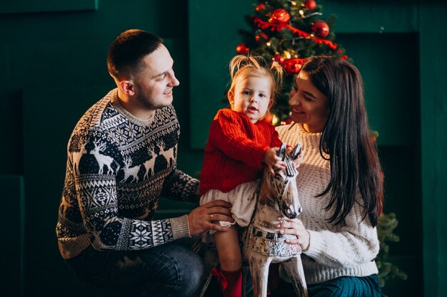 Familia con hija pequeña por árbol de Navidad jugando con pony de madera