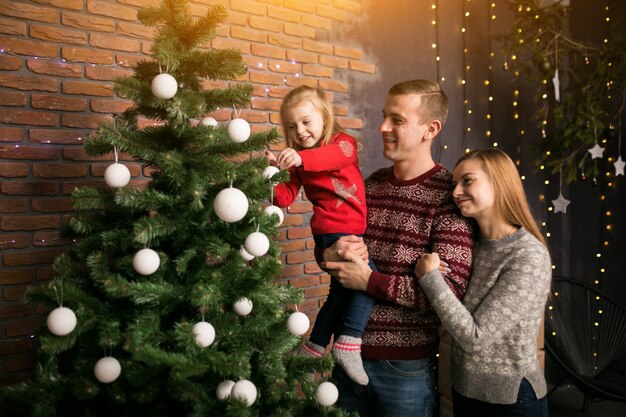 Familia con hija pequeña colgando juguetes en un árbol de Navidad