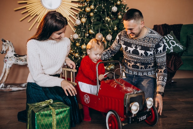 Familia con hija pequeña con regalo de Navidad por árbol de Navidad