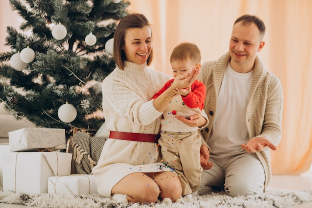 Familia con hijo pequeño por el árbol de Navidad en casa