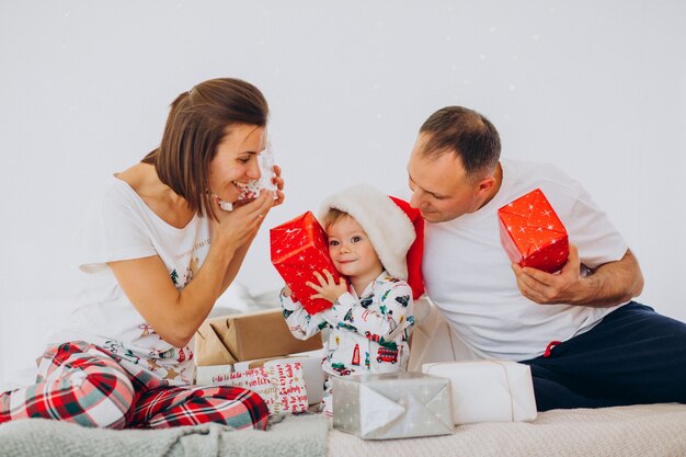 Familia con hijo pequeño y regalos de Navidad acostado en la cama