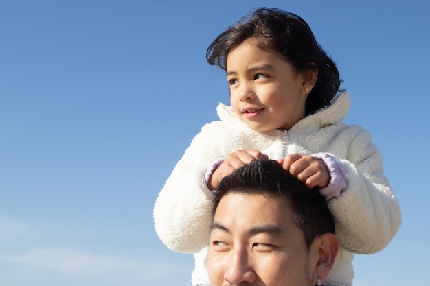 Foto gratuita familia japonesa junta en un día soleado. padre e hija jugando, cabalgando sobre los hombros. ocio, tiempo en familia, concepto de crianza.