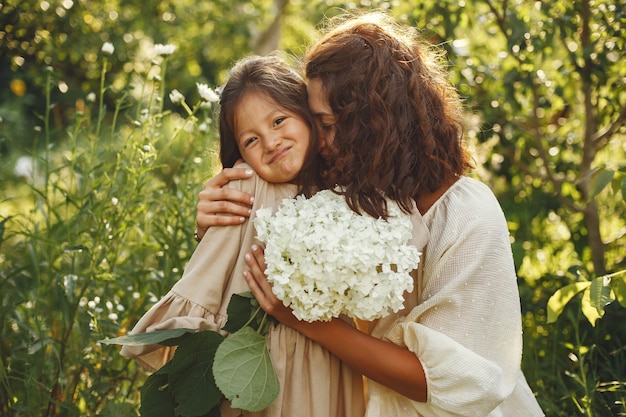 Familia en un jardín de verano. Pequeña niña bonita. Mujer con ramo.