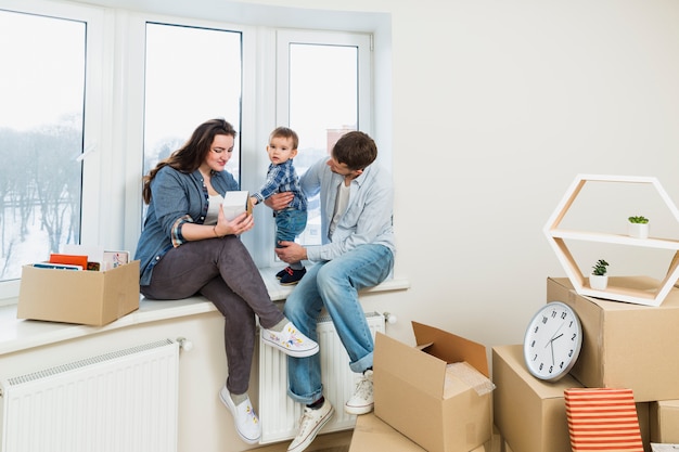 Familia joven descansando en su nuevo hogar con cajas de cartón en movimiento.