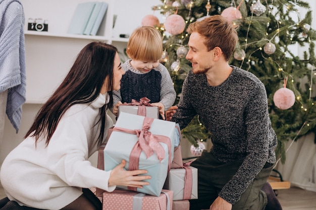 Familia joven desempacando regalos con pequeño hijo por árbol de Navidad