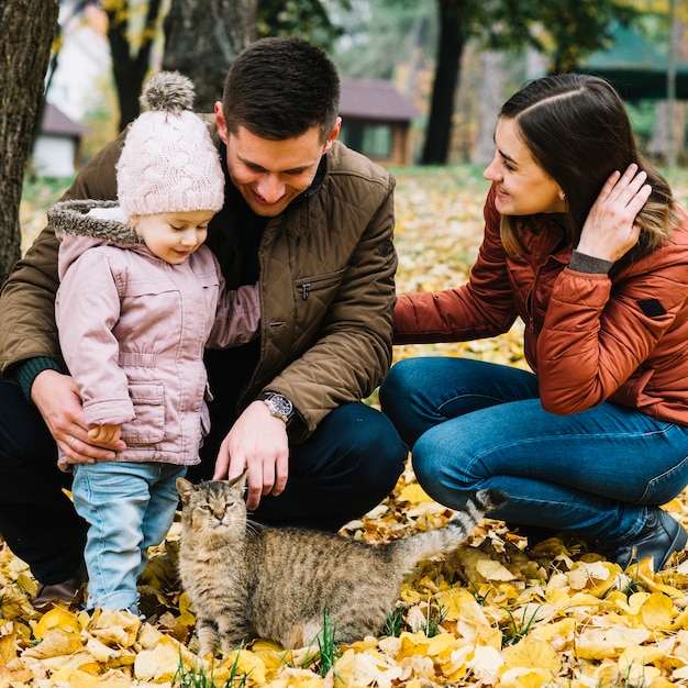 Familia joven y gato en el parque con follaje de otoño