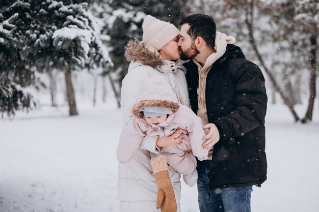 Familia joven con hija pequeña en un bosque de invierno lleno de nieve