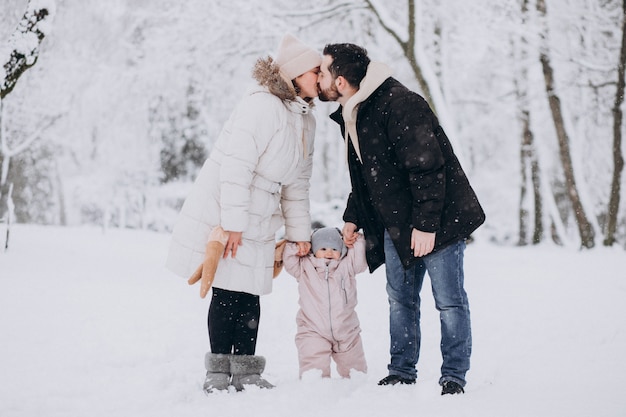 Familia joven con hija pequeña en un bosque de invierno lleno de nieve