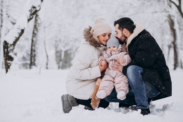 Familia joven con hija pequeña en un bosque de invierno lleno de nieve