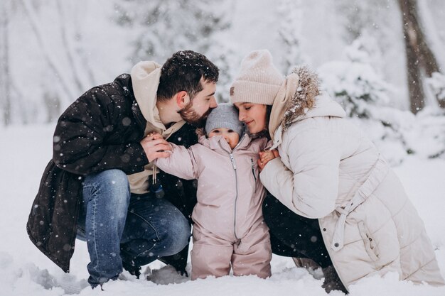 Familia joven con hija pequeña en un bosque de invierno lleno de nieve