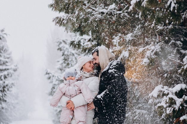 Familia joven con hija pequeña en un bosque de invierno lleno de nieve
