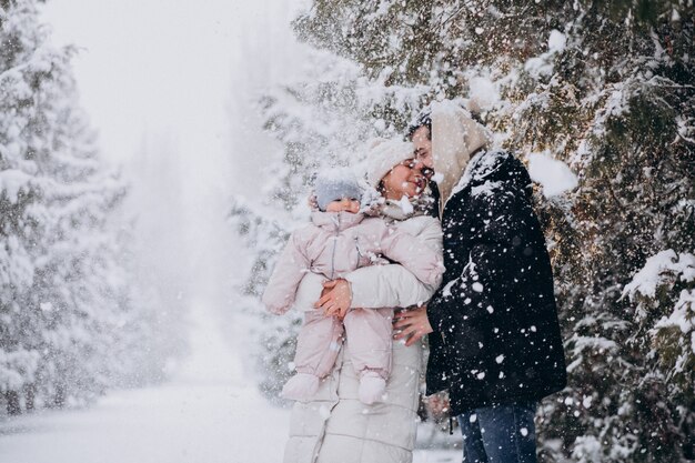 Familia joven con hija pequeña en un bosque de invierno lleno de nieve