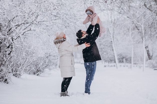 Familia joven con hija pequeña en un bosque de invierno lleno de nieve