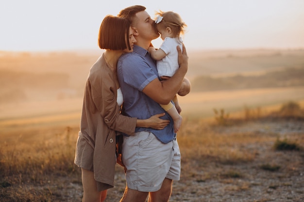 Familia joven con hija en la puesta de sol en un campo