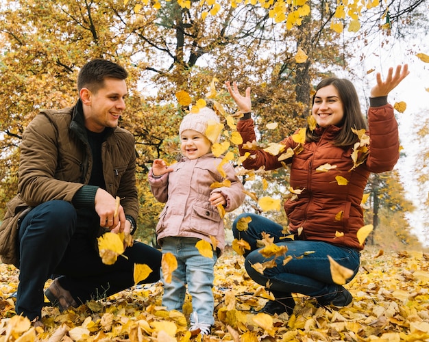 Familia joven jugando con hojas en el bosque de otoño