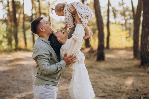 Familia joven con linda hijita caminando en el bosque en la puesta de sol