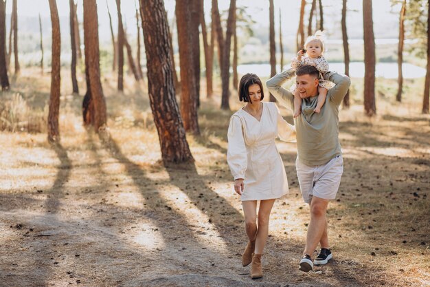 Familia joven con linda hijita caminando en el bosque en la puesta de sol