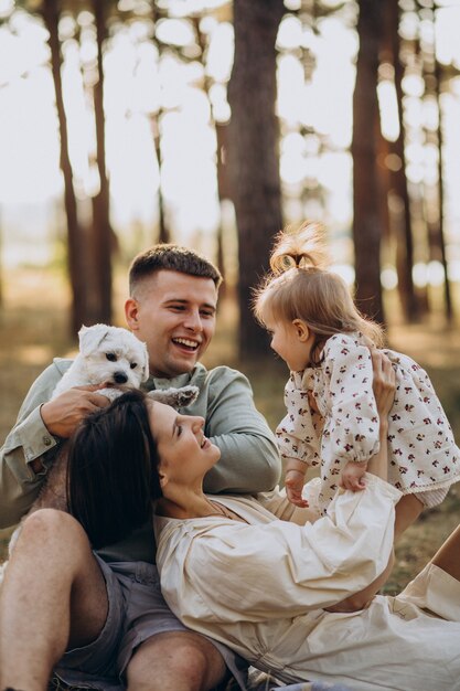 Familia joven con linda hijita descansando en el bosque en la puesta de sol