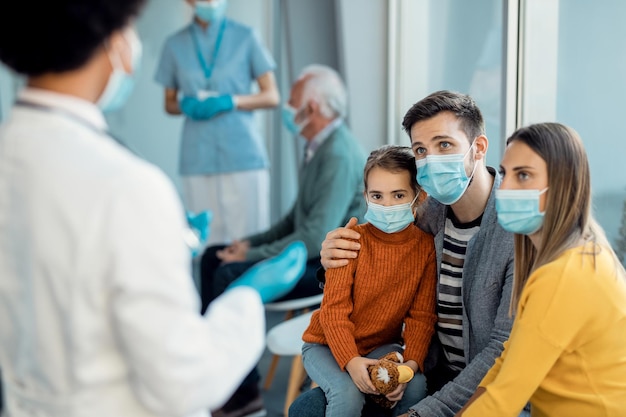 Familia joven con mascarillas protectoras hablando con un médico en una clínica médica