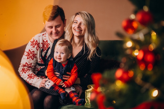 Familia joven con niña sentada junto a árbol de Navidad